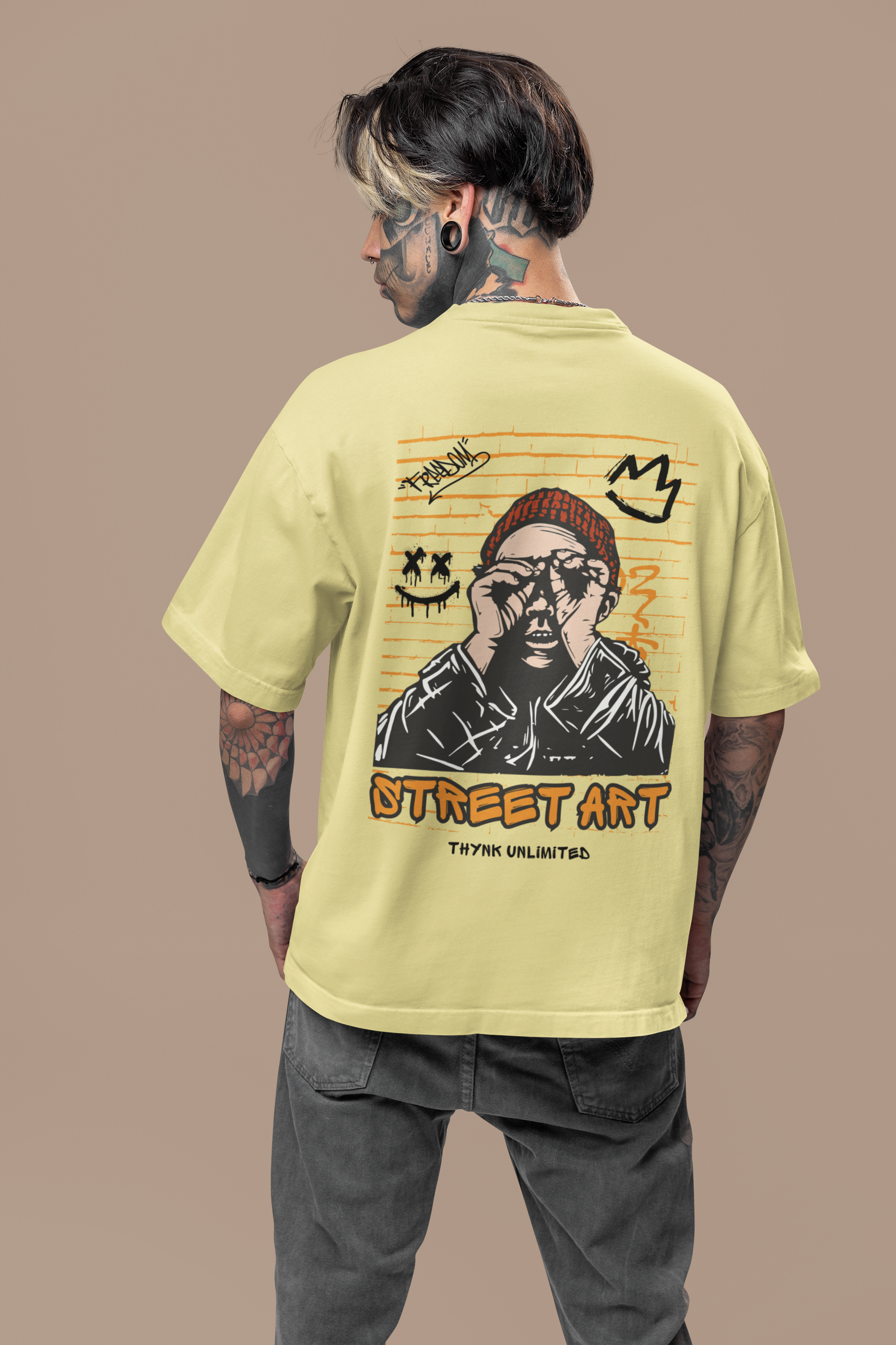 A boy wearing a beige oversized T-shirt showcasing the edgy 'Street Art' graphic design on the back, ideal for urban fashion enthusiasts by Looma Fashion.